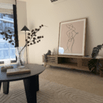 Living room with a minimalist abstract line drawing propped on a wooden console, a vase of dried branches, and a black floor lamp.