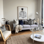 Cozy living room with a lavender sofa, cream and navy pillows, a pink throw, and a framed abstract line drawing on the wall above. A glass coffee table and a woven rug complete the scene.